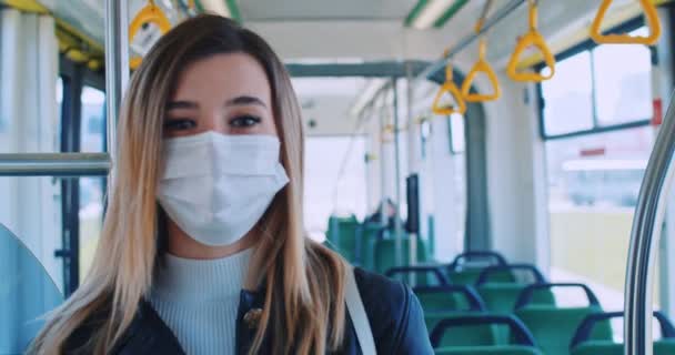 Κοντινό πορτραίτο νεαρής ξανθιάς γυναίκας με ιατρική μάσκα και γάντια που περπατάει σε άδεια μέσα μαζικής μεταφοράς. Έννοια για την υγεία και την ασφάλεια, καραντίνα coronavirus, προστασία του ιού — Αρχείο Βίντεο