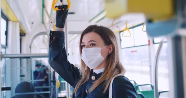 Close up portret pięknej blondynki w masce medycznej i rękawiczki zatrzymujące się w transporcie publicznym. Autobus ma niewielu pasażerów. Koncepcja bezpieczeństwa i higieny pracy, kwarantanna dla koronawirusów, ochrona wirusów — Wideo stockowe