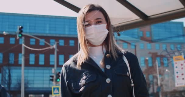 Ritratto ravvicinato di un'operaia di sesso femminile in maschera medica che soggiorna e aspetta l'autobus ad una fermata del trasporto pubblico per cercare di mettersi al lavoro in quarantena . — Video Stock