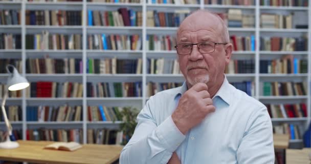 Porträt eines kaukasischen Philosophen mit Glatze, der im Bibliothekszimmer steht und mit weisem Blick denkt. Männliche Profis drehen ihr Gesicht in die Kamera und lächeln in die Kamera. Oberlehrerkonzept. — Stockvideo