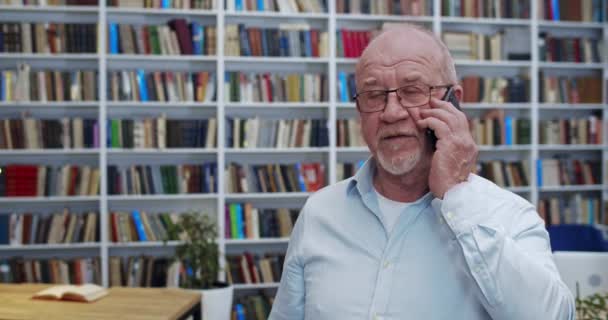 Der alte kubanische Bibliotheksangestellte mit Glatze und Brille spricht auf dem Handy. Der Senior Professor telefoniert in der Bibliotheca. Telefonat. Studienkonzept. — Stockvideo