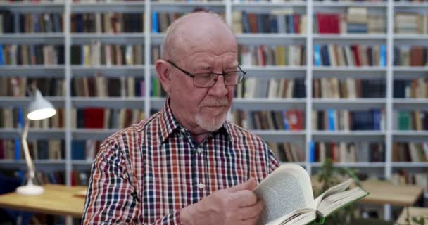 Kaukasisk flintskallig man i glasögonbok på biblioteket. Närbild av gammal manlig professor med lärobok i händerna studerar i offentlig bibliotheca. Studiekoncept. Farfar vänder blad. — Stockvideo