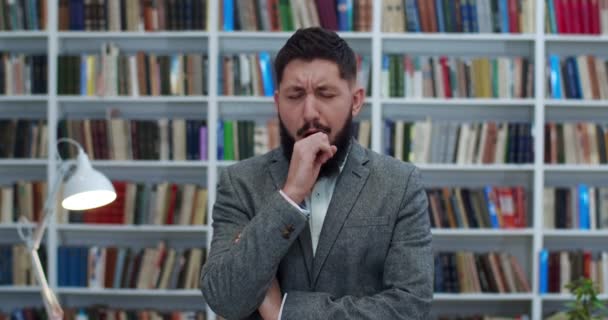 Portret van een blanke jonge zakenman met baard en gekruiste handen die in de bibliotheek staan en gapen zoals het moe is. Een mannelijke klant verveelt zich in bibliotheca. Knappe man wil slapen in boekhandel. — Stockvideo