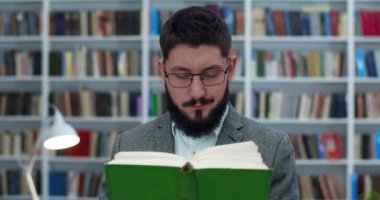 Gözlüklü, beyaz, yakışıklı bir adam kütüphanede ders kitabı okuyor. Erkek profesörü ya da araştırmacıyı elinde kitaplarla kitabevinde kitap okuyarak kapat. Konsept çalış