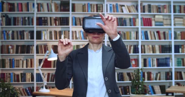 Närbild porträtt av vackra mogna kvinna bär virtuell verklighet headset röra något med hjälp av moderna 3D vr glasögon i biblioteket bredvid bokhyllan. — Stockvideo