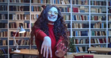 Uzun kıvırcık doğal saç çilleri ve sarı güneş gözlükleriyle kütüphanede renkli ışıklarla eğlenen sevimli kızıl saçlı öğrencinin portresi. Arkaplanda kitaplık.