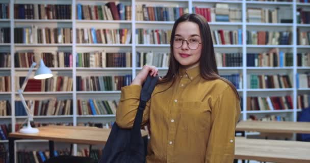 Retrato de una joven y hermosa estudiante adolescente usando su mochila después de terminar de hacer su tarea en la biblioteca . — Vídeos de Stock