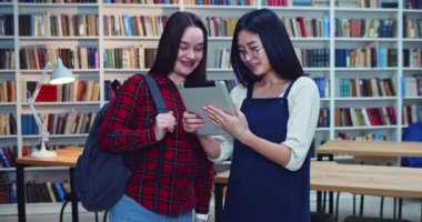 Mutlu Asyalı ve Avrupalı kızların birlikte okuduğu portre. Sınavlara hazırlanmak, kütüphanede tablet üzerine notlar yazmak.