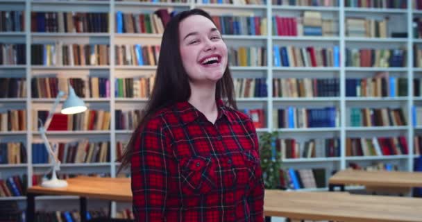 Портрет студентки брюнетки з довгим волоссям насолоджується часом і посміхається в бібліотеці . — стокове відео