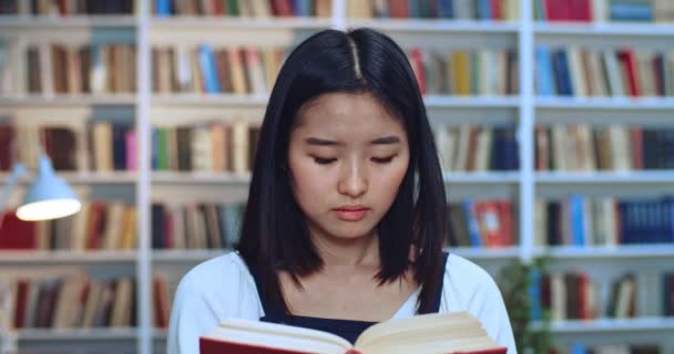 Nahaufnahme Porträt einer glücklichen asiatischen Teenie-Studentin mit schwarzem Haar, die Buch liest und in der Bibliothek laut wird. — Stockvideo