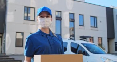 Eldivenli ve tıbbi maske takmış, elinde paketle kameranın önüne çıkan Kafkas asıllı genç kadın postacı. Dışarıda kameraya karton kutu uzatan mutlu bir kadının yakın çekimi..