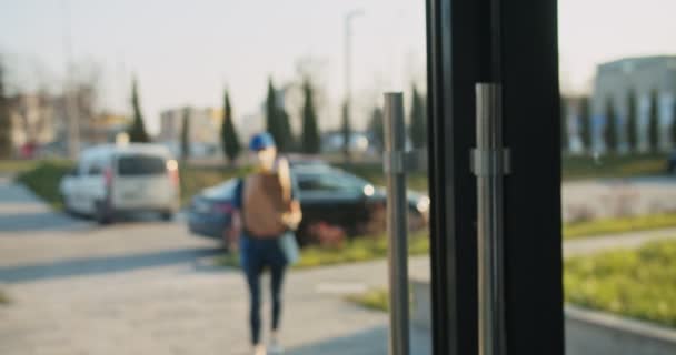 Vista posteriore sul pensionato di sesso maschile che esce dall'edificio e prende la consegna della spesa dal giovane corriere femminile caucasico. Donna in maschera e guanti che consegna il pacchetto con il cibo al vecchio. Concetto di pandemia . — Video Stock