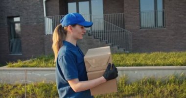 Caddede yürüyen ve elinde iki karton kutu taşıyan genç, beyaz bir kurye. Açık havada. Karton kutular taşıyan güzel bir kadın. Konsept sunma.