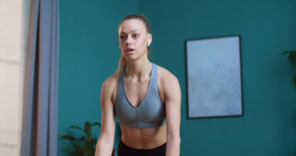 Retrato de una joven deportista haciendo ejercicio físico con pesas en las manos. La chica está construyendo su cuerpo y manteniéndose en forma en casa. Deporte y fitness. Concepto de entrenamiento, entrenamiento y bienestar . — Vídeo de stock