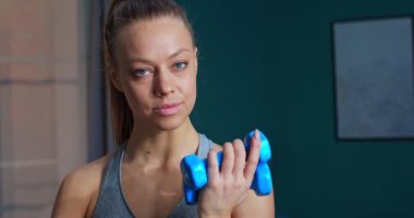 Güneşli bir günde yoğun spor yaptıktan sonra dambılları kaldıran ve kameraya bakan güzel, genç ve formda bir kadının portresi. Spor ve spor. Eğitim, egzersiz ve sağlık konsepti.