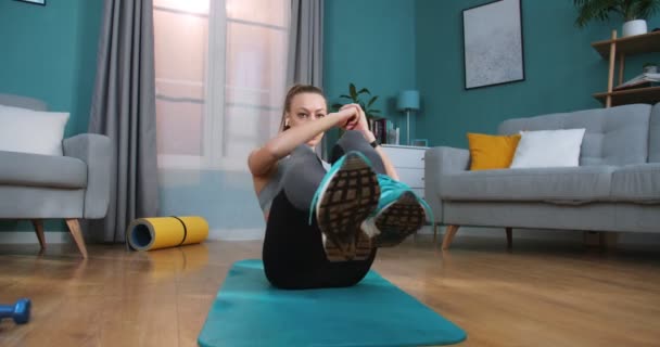 Vrouwelijke fitnesstrainer in atletisch topje doet buikoefeningen in een modern appartement. Fit vrouw doen buikspieren oefeningen buigen benen op de vloer thuis. Fitness, thuis-, trainings- en voedingsconcept. — Stockvideo