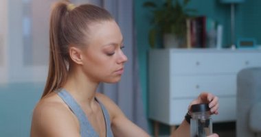 Güzel, genç ve zinde bir kadının portresi yoğun spor antrenmanından ve içme suyundan sonra evde yerde oturuyor. Spor ve spor. Eğitim, egzersiz ve sağlık konsepti.