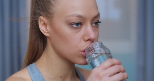 Portret van een schattige jonge en fitte vrouw thuis na intensieve sporttraining en het drinken van water uit de fles en op zoek naar camera. Sport en fitness. Training, training en wellness concept. — Stockvideo