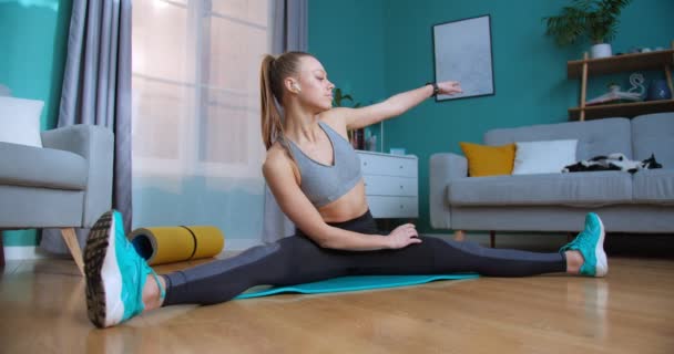 Mujer joven haciendo ejercicio en casa con reloj inteligente en la hermosa sala de estar moderna durante la cuarentena. Deporte y fitness. Concepto de entrenamiento, entrenamiento y bienestar . — Vídeos de Stock