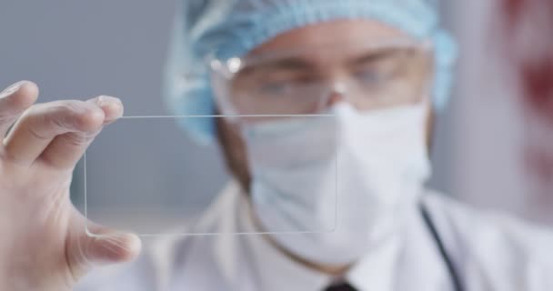 Retrato de primer plano del científico mirando las células sanguíneas en el fondo de la medicina, usando máscara médica, guantes. Tecnología futurista, holograma de datos saludable, pandemia, concepto de medicina moderna . — Vídeo de stock
