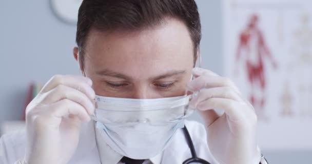 Retrato de close-up de médico profissional com estatoscópio, brilho e máscara médica usando óculos. Terapeuta masculino em proteção respiratória no armário. Pandemia, medicina, conceito de vírus corona . — Vídeo de Stock