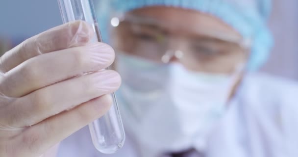 Close-up portrait of handsome blue-eyed geneticist wearing protection clothes making experiment using test tubes in a big modern laboratory. Lab worker doing chemical experiment in laboratory. — Stock Video