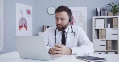 Çevrimiçi doktor danışmanlığı. Aile terapisti kabinede masada oturuyor ve web kamerasıyla hastaya danışmanlık yapıyor. Video kaseti olan bir adam, karantina sırasında tıbbi danışmanlık yapıyor..