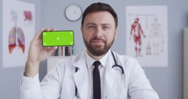 Doktor, hastane odasında krom anahtarlı bir telefon, mavi gözlü yakışıklı bir adamın portresi, steteskoplu, yeşil ekranlı, yatay bir akıllı telefon..