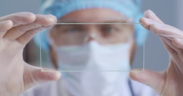 Detailní portrét pohledného futuristického lékaře, chirurga, který se dívá na technologickou digitální holografickou desku, používá lékařskou masku, rukavice. Pojem futuristická medicína, lékaři, budoucí laboratorní obor — Stock video