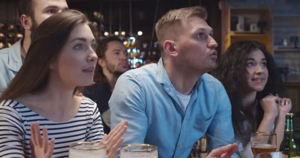 Kaukasiska manliga och kvinnliga vänner tillbringar kvällen i baren när du tittar på sport spel. Män och kvinnor klappar och ger fem efter mål. Fotbollsfans titta på match på TV med öl i puben och jubel. — Stockvideo