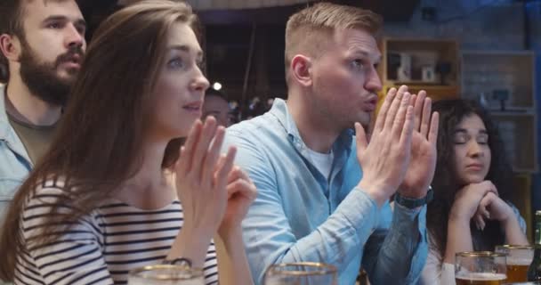 Blanke vrienden, mannen en vrouwen die de nacht doorbrengen in een bar en sport kijken. Jongens en meisjes maken zich zorgen en wachten. Voetbalfans kijken wedstrijd op tv in pub en is boos en teleurgesteld na losse. — Stockvideo