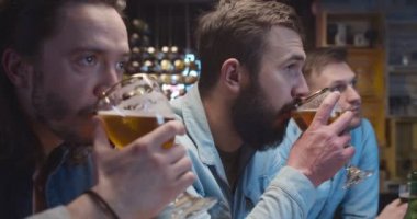 Kafkasyalı erkekler ve akşamları birayla barda oturup TV 'de spor kanalı izliyorlar. Arkadaşlar barda futbol hakkında konuşuyor ve tartışıyorlar. Neşeli erkekler bira içiyor.