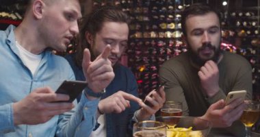 Beyaz erkek, yakışıklı futbol hayranları barda maç izliyor ve cep telefonlarından mesaj yolluyorlar. Maç sonuçlarına bahis oynayan adamlar. Erkekler barda bahisçi oranlarını cep telefonlarıyla artırıyor.