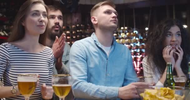 Amigos caucásicos viendo el juego deportivo y apoyando a diferentes equipos. Chicos y chicas preocupados y esperando. Los aficionados al fútbol frente a la televisión en el pub son felices y molestos, alegres y decepcionados . — Vídeos de Stock