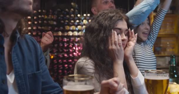 Male and female Caucasian friends watching sport match together on TV channel in pub. People celebrating scoring goal or victory of their team and girl is sad and dissapointed of loose or missing goal — Stock Video