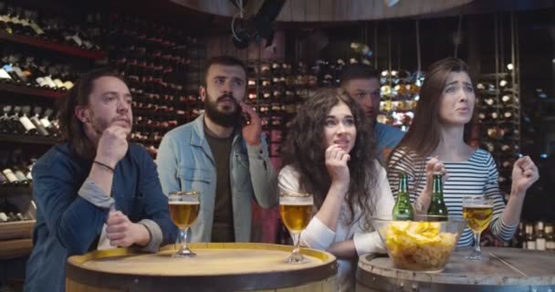 Amis masculins et féminins caucasiens passent la soirée au bar en regardant le jeu de sport. Hommes et femmes sont déçus que l'équipe manque un but ou perdre. Les fans de football regardent le match à la télévision avec de la bière au pub . — Video