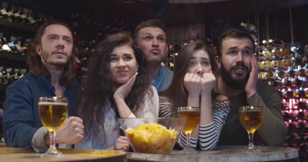 Jóvenes aficionados al fútbol masculino y femenino viendo el juego juntos en la noche en el pub y animando a su equipo favorito. Caucásicos amigos están molestos y decepcionados de fútbol suelto en el bar . — Vídeos de Stock