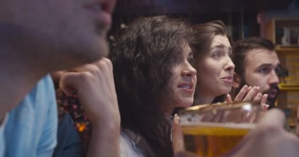 Meninas e rapazes, fãs de futebol assistindo jogo juntos à noite no pub e se preocupar com sua equipe favorita. Jovens e mulheres caucasianas animando e celebrando o resultado do jogo em bar . — Vídeo de Stock