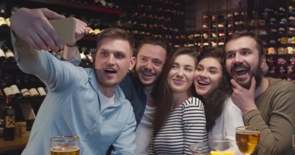 Caucásico amigos masculinos y femeninos tomando foto selfie con la cámara del teléfono en el bar al ver el juego deportivo. Hombres y mujeres haciendo fotos en smartphone y sonriendo en el pub. Los aficionados al fútbol ven TV con cerveza . — Vídeos de Stock