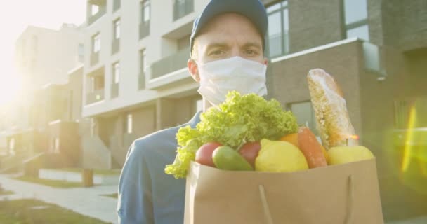 Portret kuriera noszącego czapkę i maskę medyczną ze świeżą żywnością. Kurier przynoszący zakupy do domu, dostawa od drzwi do drzwi podczas kwarantanny. Zamów produkty online, zostań w domu. — Wideo stockowe