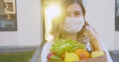 Tıbbi maske takmış, elinde market paketi olan beyaz, güzel, mutlu bir kadının portresi. Bir paket organik yiyecekle kameraya gülümseyen bir kız. Markette güzel bir kadın..