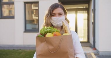 Kafkasyalı güzel, mutlu bir kadının portresi. Tıbbi maske takmış, elinde market paketi var. Bir paket organik yiyecekle kameraya gülümseyen bir kız. Markette güzel bir kadın..