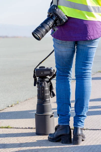 Photographer stands with modern digital camera and big telephoto lens on event outdoor.