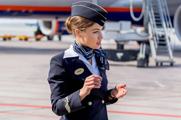 Rusya, Vladivostok, 10/13/2017. Güzel hostes Aeroflot Havayolları havaalanı üzerinde resmi koyu mavi üniforma giymiş. Arka plan üzerinde yolcu jet uçağı. Uçağının mürettebatı. Havacılık ve ulaşım.