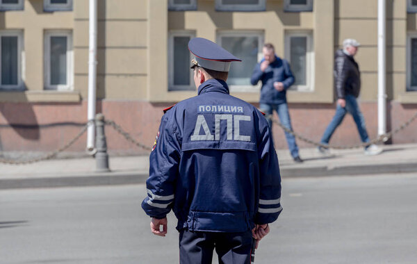 A policeman watches the walking people in city downtown. Inscription "Police" on uniform jacket. Russia, Vladivostok.