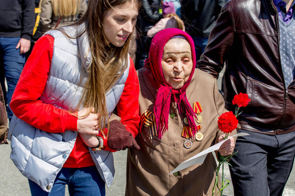 Russia, Vladivostok, 05/09/2018. Old woman, veteran and hero of Great Patriotic War between USSR and Nazi Germany (1941-1945). Volunteer helps her to move. Annual Victory Day on May'9.