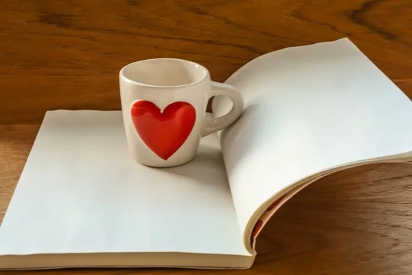 Beyaz fincan beyaz kitap ahşap masa üzerinde kırmızı kalpli Kupası ile seçici odak arka plan bulanıklık