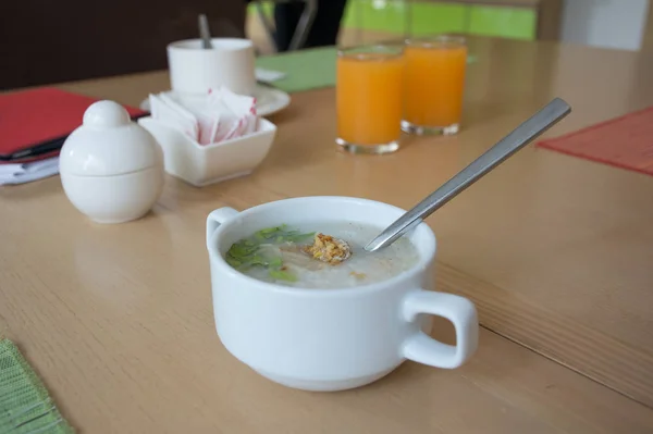 Healthy chicken rice soup in a white cup with a spoon placed on a wooden table