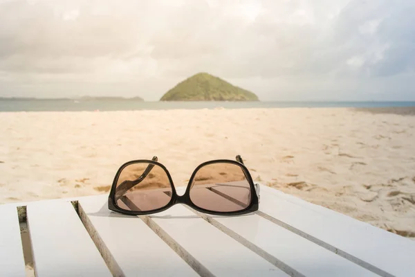 Siyah güneş gözlüğü olduğunu plaj arka plan ve güneşli ışık Beyaz ahşap masa yüzünde sabah