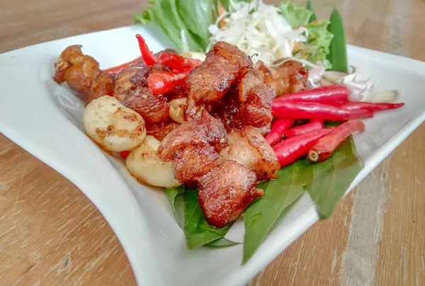 Tay gıda tuz kavrulmuş domuz (Moo Kua Kleu) beyaz plaka ile kahverengi ahşap masa, Phuket, Tayland için popüler yerel gıda